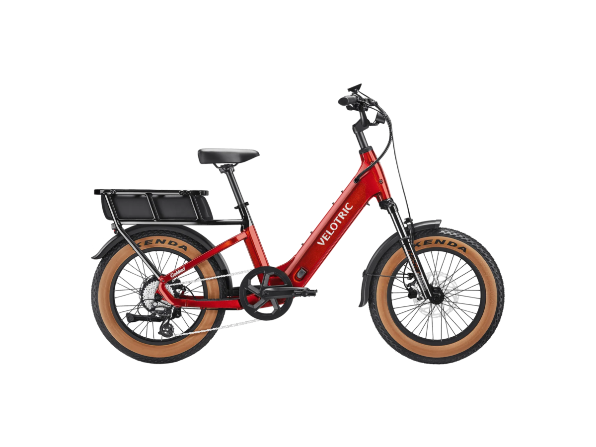 Red Velotric electric bike with tan-wall tires, front suspension, and rear cargo rack on a white background.